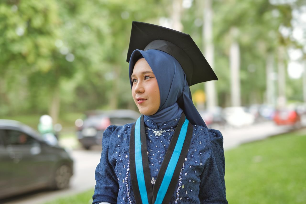 Young woman in hijab wearing a graduation cap, celebrating achievement outdoors.