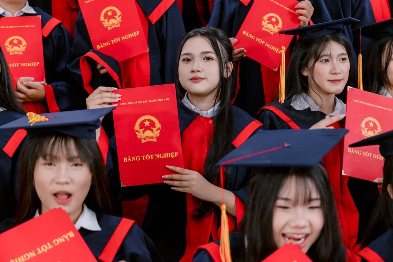 Graduates in gowns proudly holding Vietnamese diplomas at a ceremony.